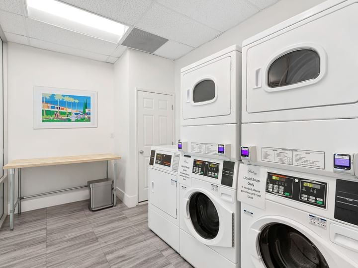 A hotel laundry room with white walls, gray floor, and stacked washer and dryer units.
