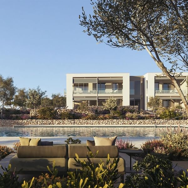 Albergo moderno con piscina e divani esterni, circondato da piante e alberi, sotto un cielo blu.