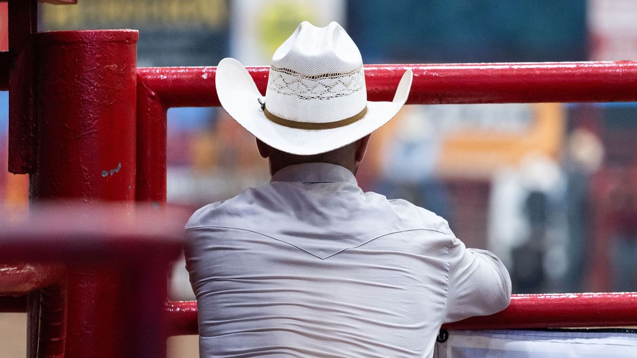 man in a cowboy hat leaning on a red fence