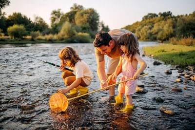 Man and two young children wearing yellow boots are playing and fishing with nets near Fall Creek Marina & Campground