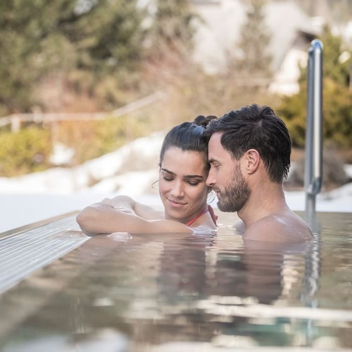 Lächelndes Paar im Whirlpool entspannt sich bei Falkensteiner Hotel Schladming