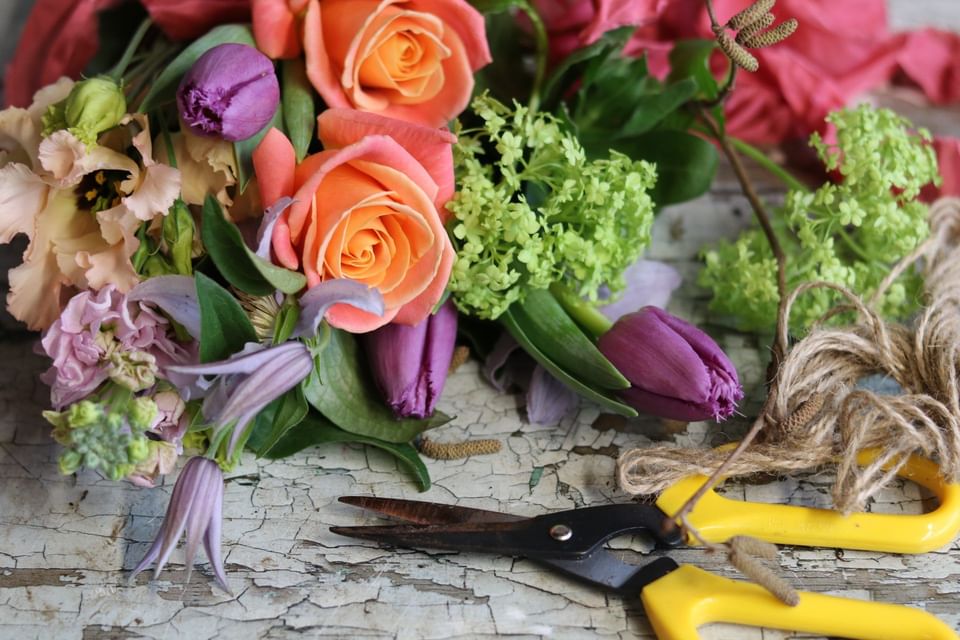 Fresh flower bouquet with orange roses and purple tulips beside yellow pruning shears on a wood table at Hotel X Toronto