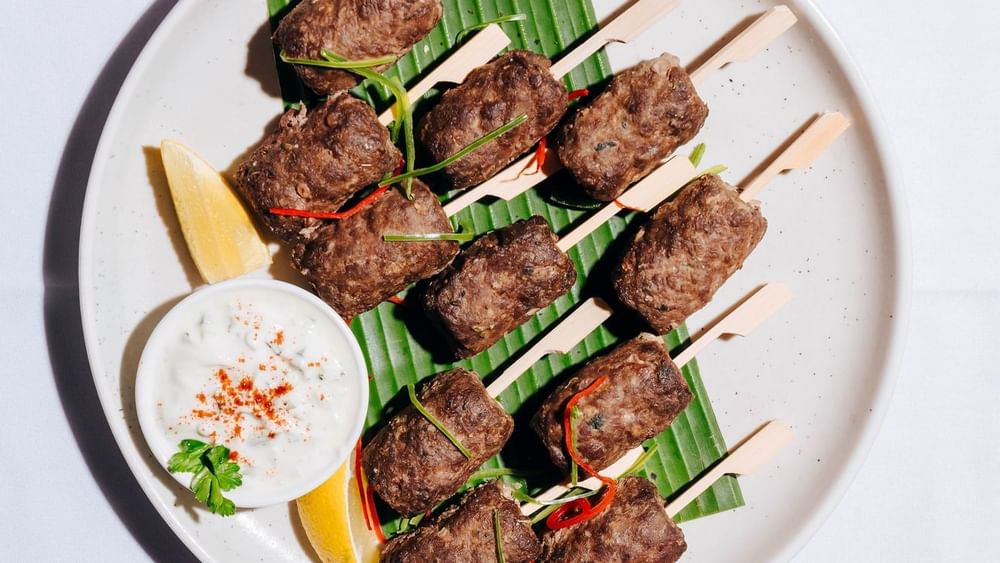 Plate of grilled skewers with seasoned meat served with a side of creamy dip in The Lounge at Novotel Sydney Olympic Park