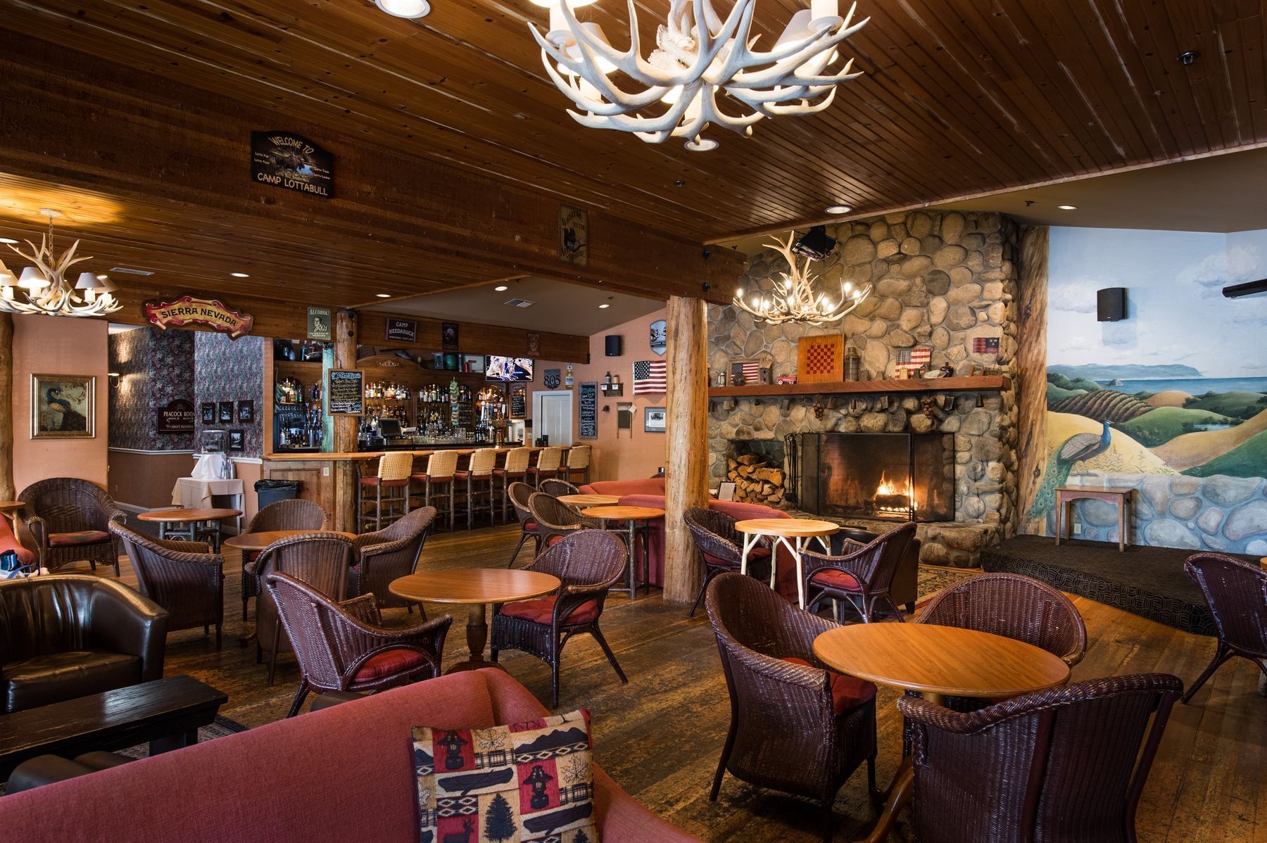 A cozy lounge area with a stone fireplace, wooden beams, and an antler chandelier.