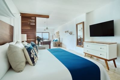 Elegant bedroom with large bed, blue blanket, pillows, TV, and a living area with couch and balcony view.