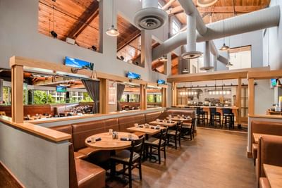 Leather booths and wooden tables with coffee mugs under a wooden beam ceiling in ML Steaks & Sports at Miami Lakes Hotel