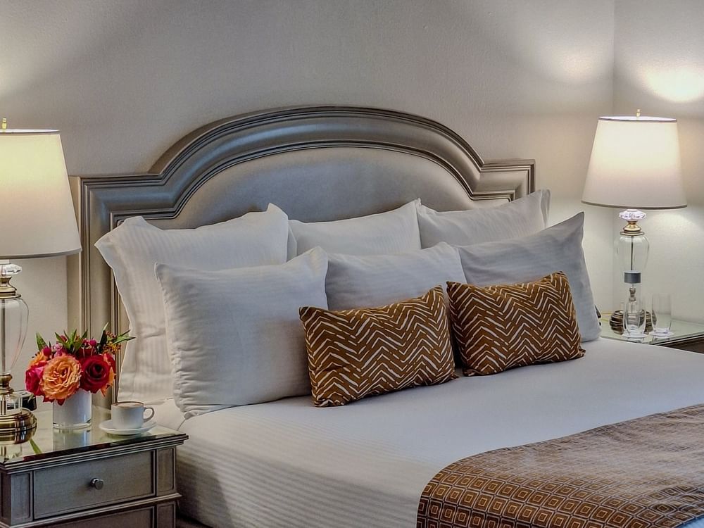 King bed with bronze pillows by a side table under a bedside lamp in Classic King Accessible at Warwick Melrose Dallas