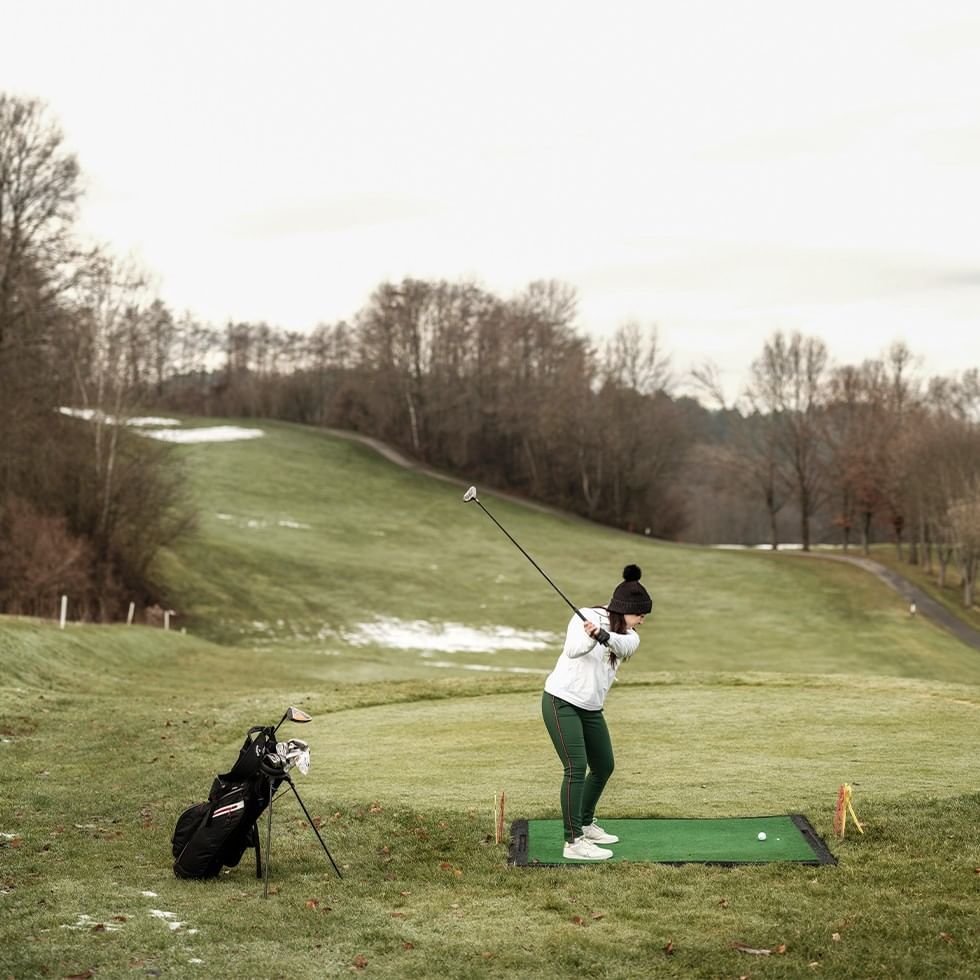 Golfista donna in abbigliamento invernale che colpisce una palla da golf sul campo da golf.