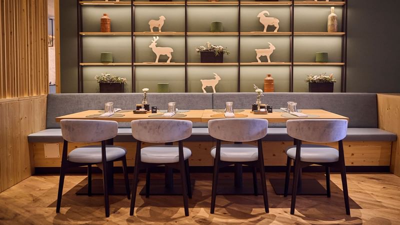 Esstisch mit vier Stühlen vor einer Wand mit Regalen und Tierfiguren, neben einer Bank.