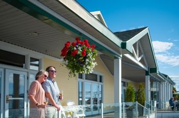 Couple standing on a patio under a hanging flower basket at Rodd Miramichi River, one of the best hotels in Miramichi, NB