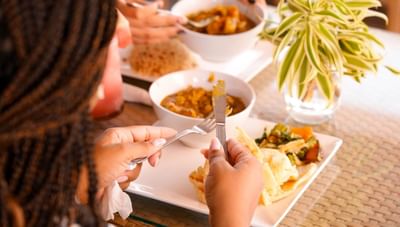 Person holding a fork and knife with breakfast food and fresh curry in Hott Pott Restaurant at Worthing Court Apartment