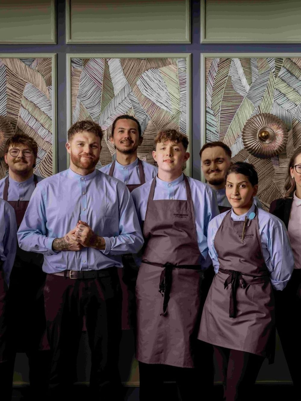 Uniformed restaurant staff posing by patterned wall panels at The Capital Hotel, Apartments and Townhouse