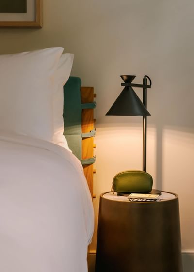 Close-up of a bed, round nightstand, modern black lamp, and green leather purse in Bedroom Queen at Kenmore Village Hotel