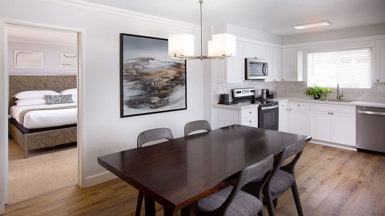 A kitchen and bedroom with a dining table, chandelier, microwave, refrigerator, and bed.