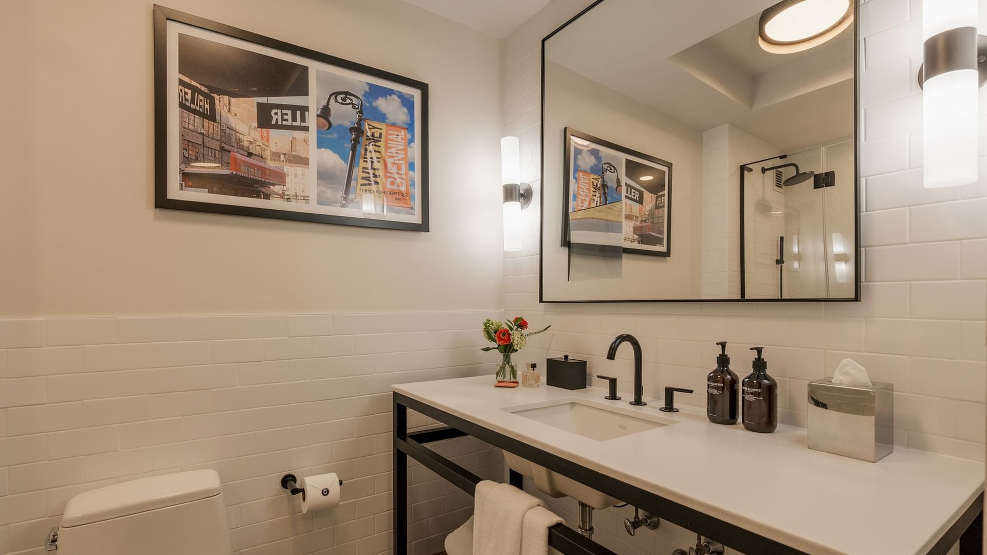 Modern bathroom with white subway tile, black fixtures, and framed artwork in the Two-Bedroom Gansevoort Suite at Gansevoort Meatpacking NYC.
