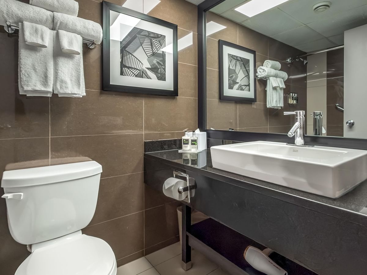 Modern bathroom with white vessel sink, brown tile walls, and framed artwork at Coast Calgary University Area Hotel by APA