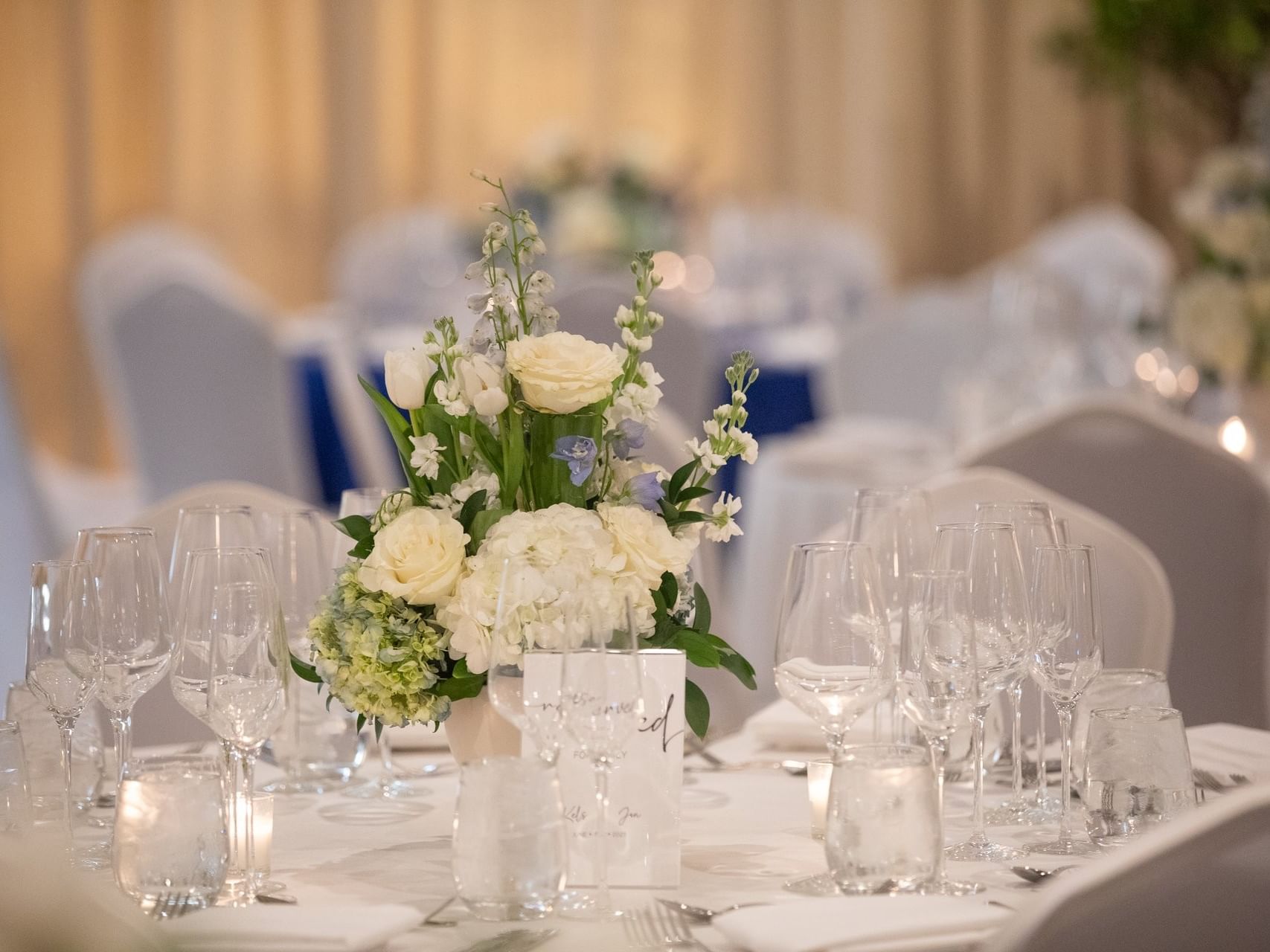 Centro de mesa floral blanco sobre una mesa de comedor formal, rodeado de copas de vino, en el «Monet Foyer» del Grand Beach Hotel Surfside
