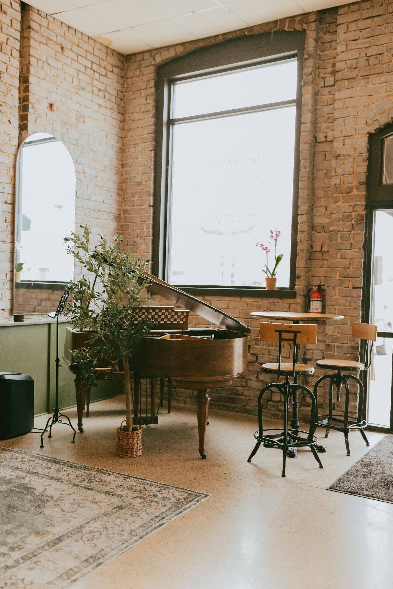 A lobby with a piano, table, chairs, and plant