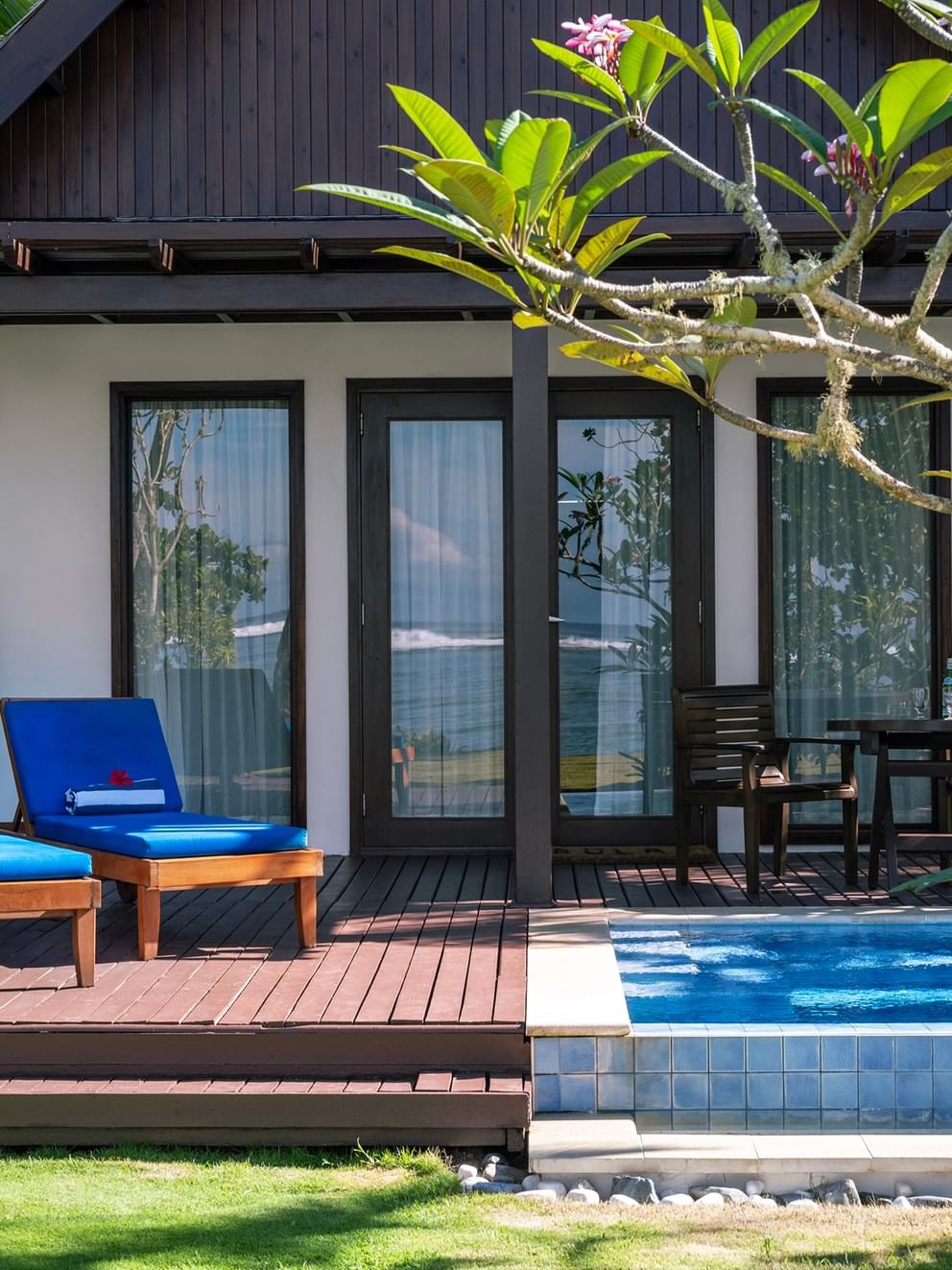 Blue lounge chairs by a private pool on a wooden deck under a leafy tree at Tambua Sands Beach Resort