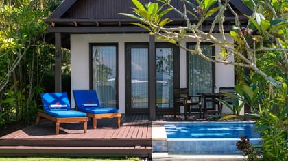 Blue lounge chairs by a private pool on a wooden deck under a leafy tree at Tambua Sands Beach Resort