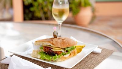 Burger with cheese and lettuce on a bun beside a white dipping sauce and wine at Worthing Court Apartment
