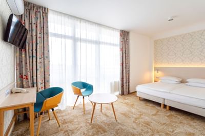 Bedroom with double bed, work desk, TV & chair near window in Junior Suite at Metropol Hotel