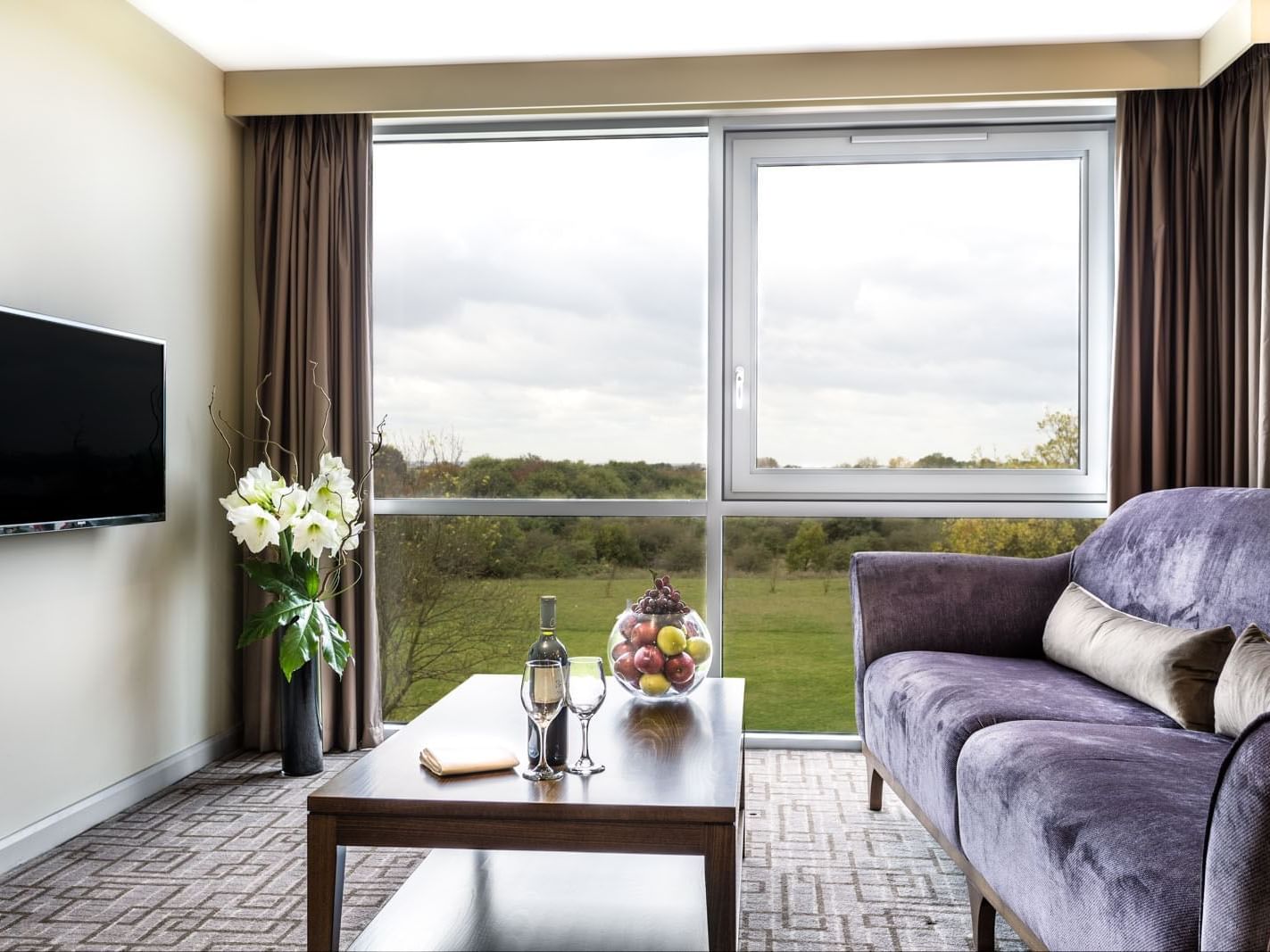 TV lounge with plush seating by the window and carpet floors in the One Bedroom Suite at Heston Hyde Hotel