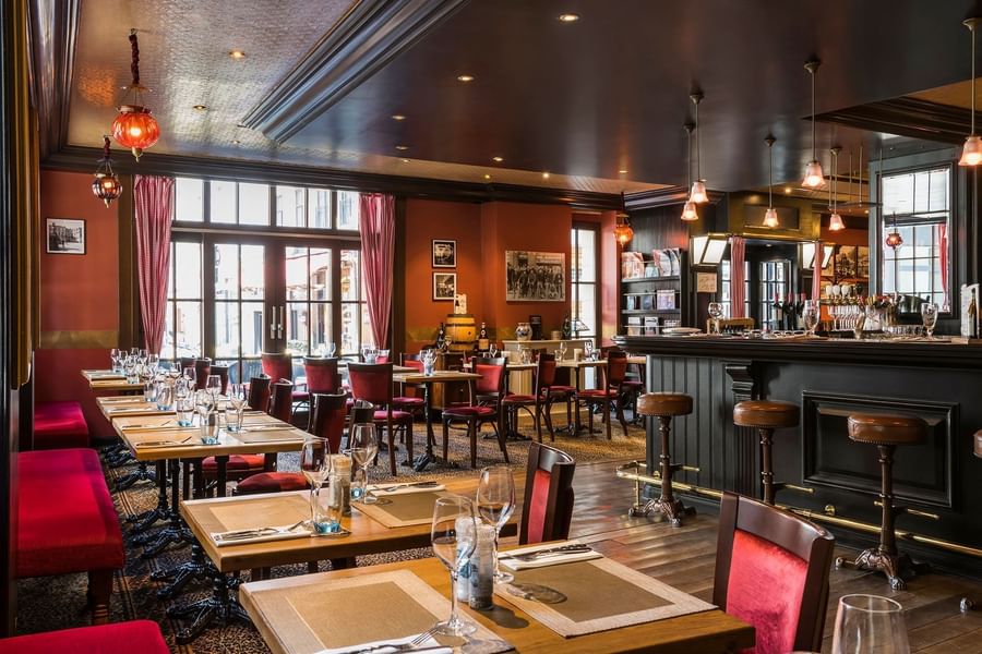Dining tables set with glasses beside a dark bar counter and red booth seating at The Chutney\’s Restaurant