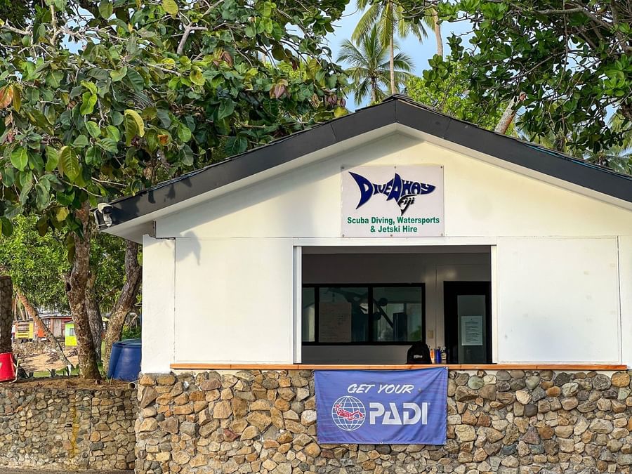 Dive shop booth by a stone wall under lush green trees at The Naviti Resort in Korolevu