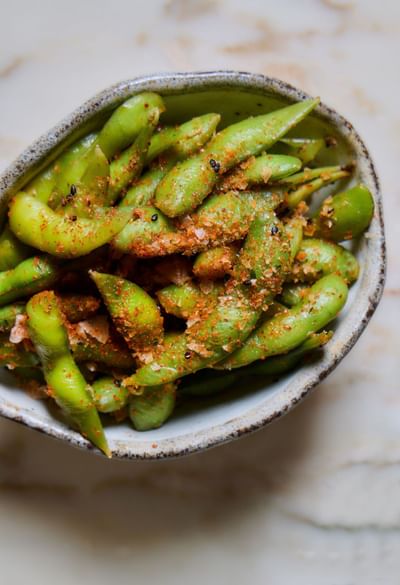 Green edamame beans in a bowl topped with seasoning and salt at May Fair Kitchen