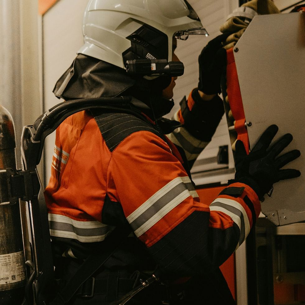 Firefighter in safety gear and helmet fixing a cabinet with tools and fire extinguisher nearby.