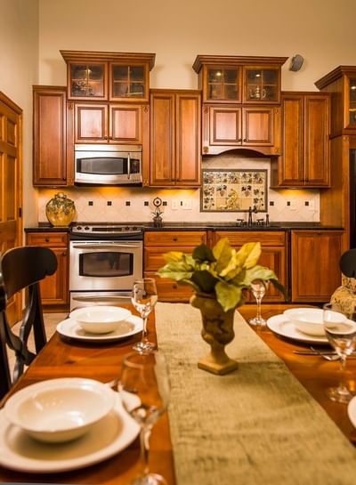 A dining table set with plates and glasses in a kitchen with wooden cabinets and a stovetop at The Stanley Hotel