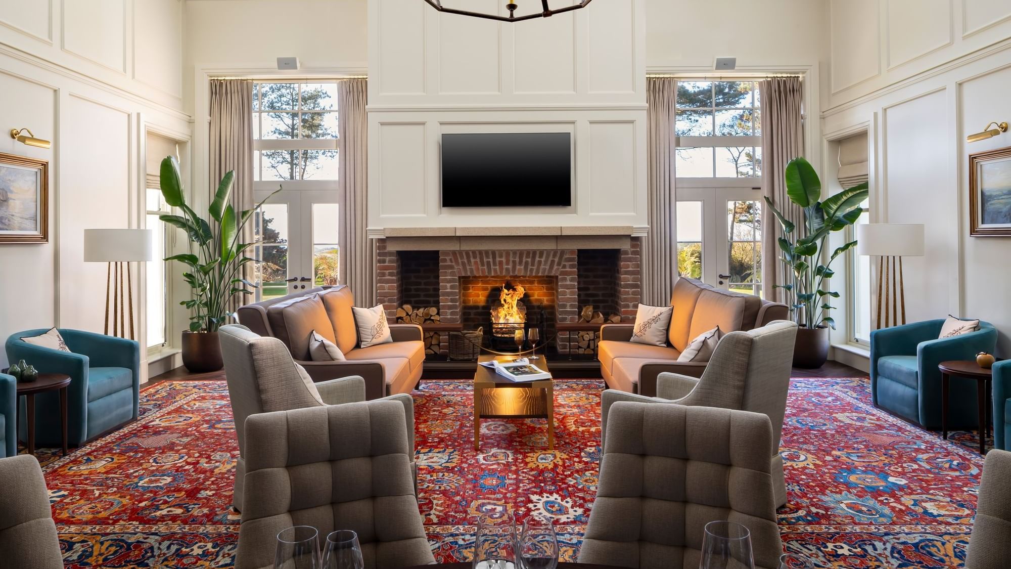 The Stookan lounge with a lit fireplace, two brown sofas, and two grey armchairs on a red patterned rug at Dunluce Lodge