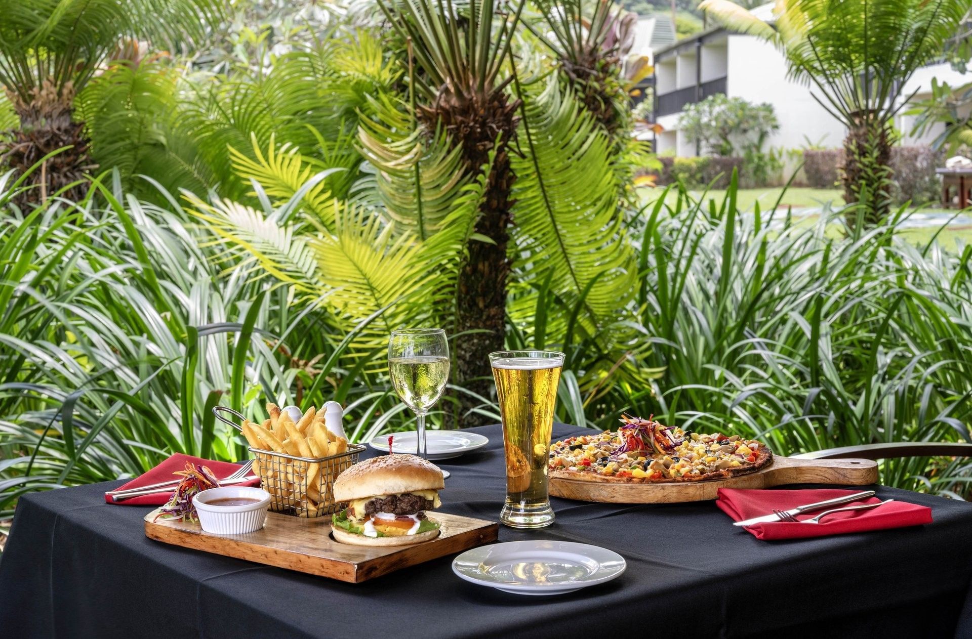 Burger and pizza on a table by beer and wine under lush palms at The Naviti Resort - Fiji