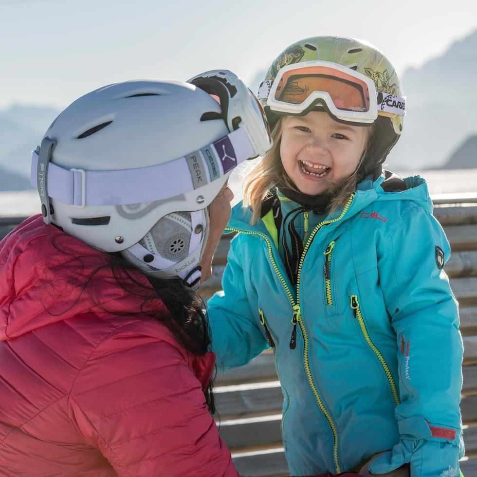 Großmutter und Enkelin in Skiausrüstung lächelnd bei Familienzeit mit Oma & Opa.