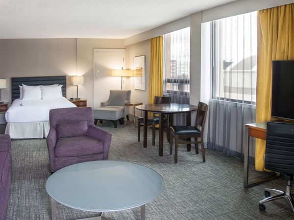 A hotel suite with a queen bed, living area with a desk, and a balcony.