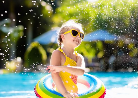 Little girl in a yellow swimsuit & sunglasses having fun in the outdoor pool at Gorges Grant Hotel