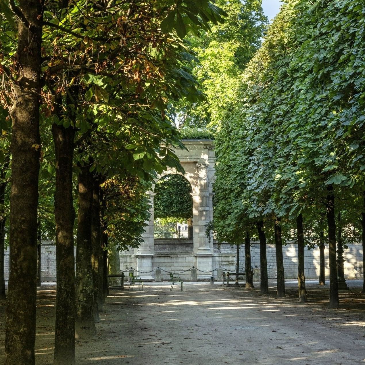 Un allée bordée d'arbres mène à une arche dans le Jardin des Tuileries.