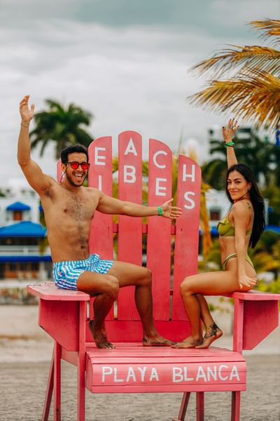 Couple posing by a big Beach Vibes chair at Playa Blanca Beach Resort