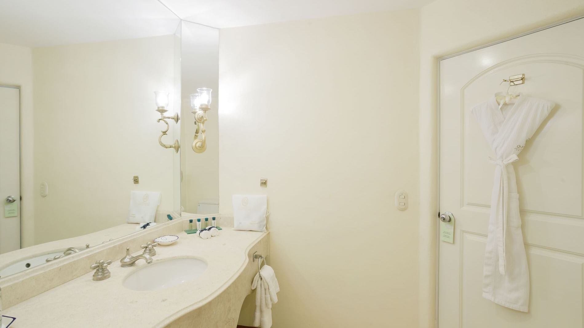 2 Double Grand Class vanity area featuring a large mirror and a plush white robe on the door at Quinta Real Acapulco