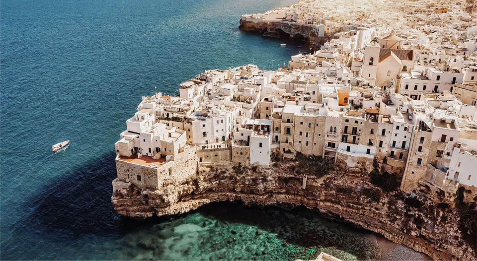 Aerial view of whitewashed coastal buildings perched on rocky cliff above turquoise sea in Apulia near Meraviglia