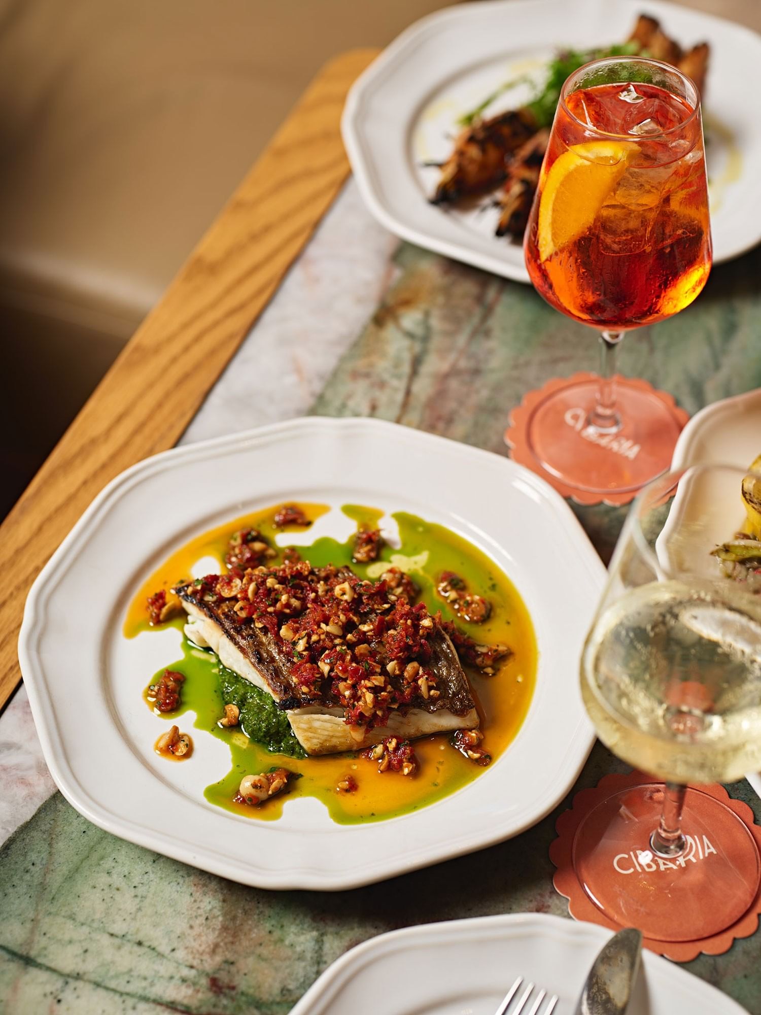 Elysium Manly seared fish plated in citrus sauce by an Aperol spritz and wine, best 5-star hotels in New South Wales