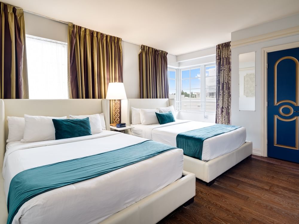 A hotel room with two beds, white bedding, and teal accents.
