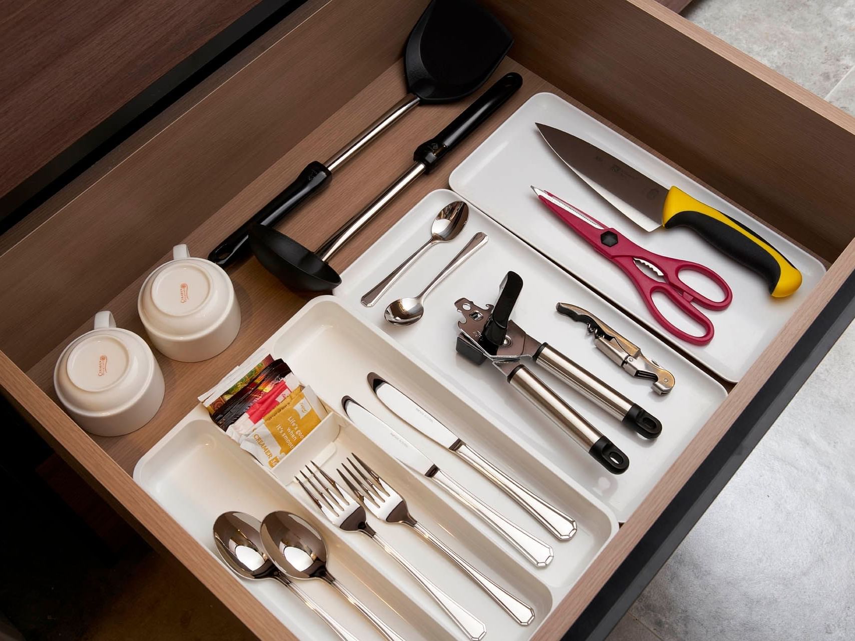 Neatly organized kitchen drawer with utensils, cutlery, measuring spoons, and cups at Orchard Grand Court