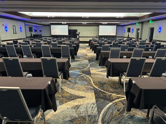 Classroom seating with blue chairs and covered tables facing two screens in the Grand Slam Ballroom at Miami Lakes Hotel
