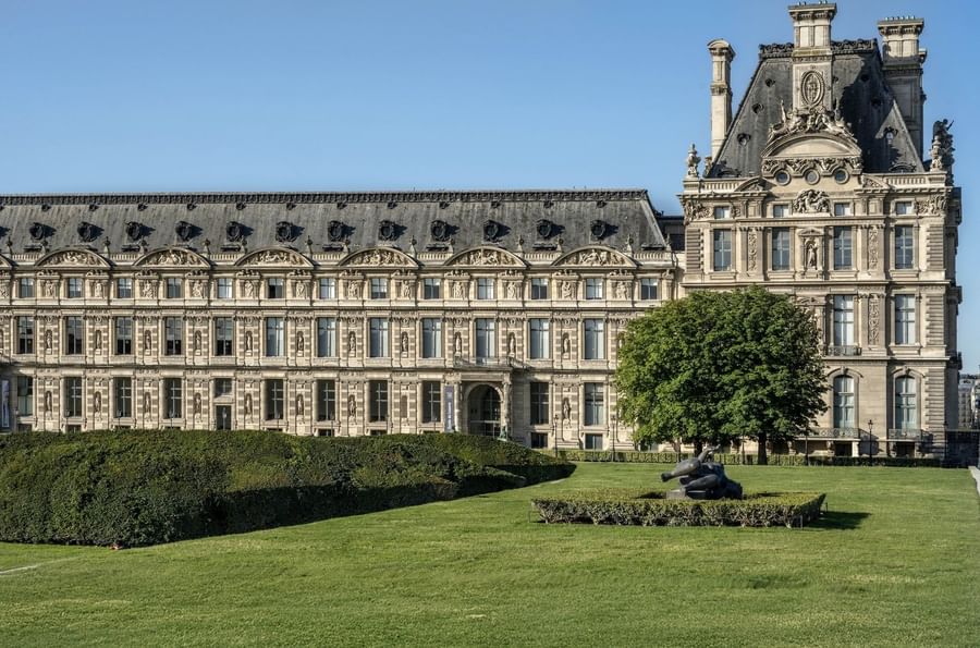 Louvre Museum facade with a green lawn and sculpture placed by a large tree near Hotel Westminster Paris