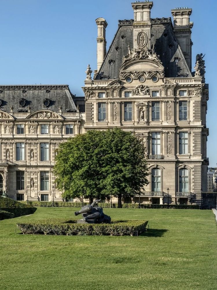 Louvre Museum facade with a green lawn and sculpture placed by a large tree near Hotel Westminster Paris