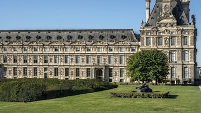 Louvre Museum facade with a green lawn and sculpture placed by a large tree near Hotel Westminster Paris