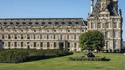 Louvre Museum facade with a green lawn and sculpture placed by a large tree near Hotel Westminster Paris