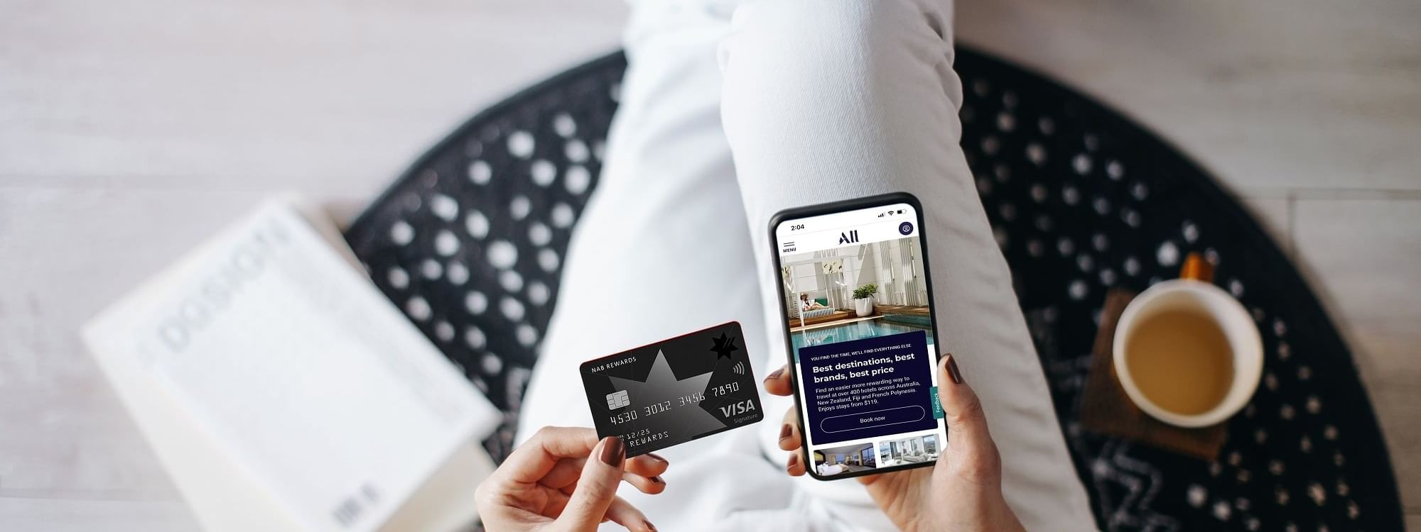 Top view of a lady holding a smartphone displaying a booking site of ALL and NAB rewards card at Novotel Sydney Olympic Park